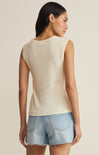 Woman wearing a beige sleeveless top and denim shorts on a plain background