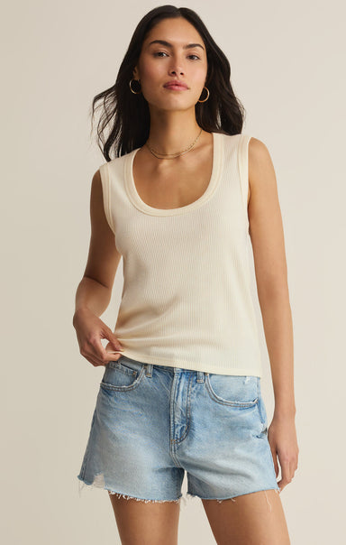 Woman wearing a beige tank top and denim shorts on a plain background