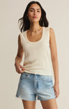Woman wearing a beige tank top and denim shorts on a plain background