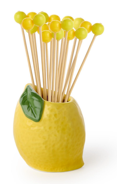 Yellow ceramic holder with lemon design containing wooden sticks and green balls on a white background