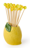 Yellow ceramic holder with lemon design containing wooden sticks and green balls on a white background