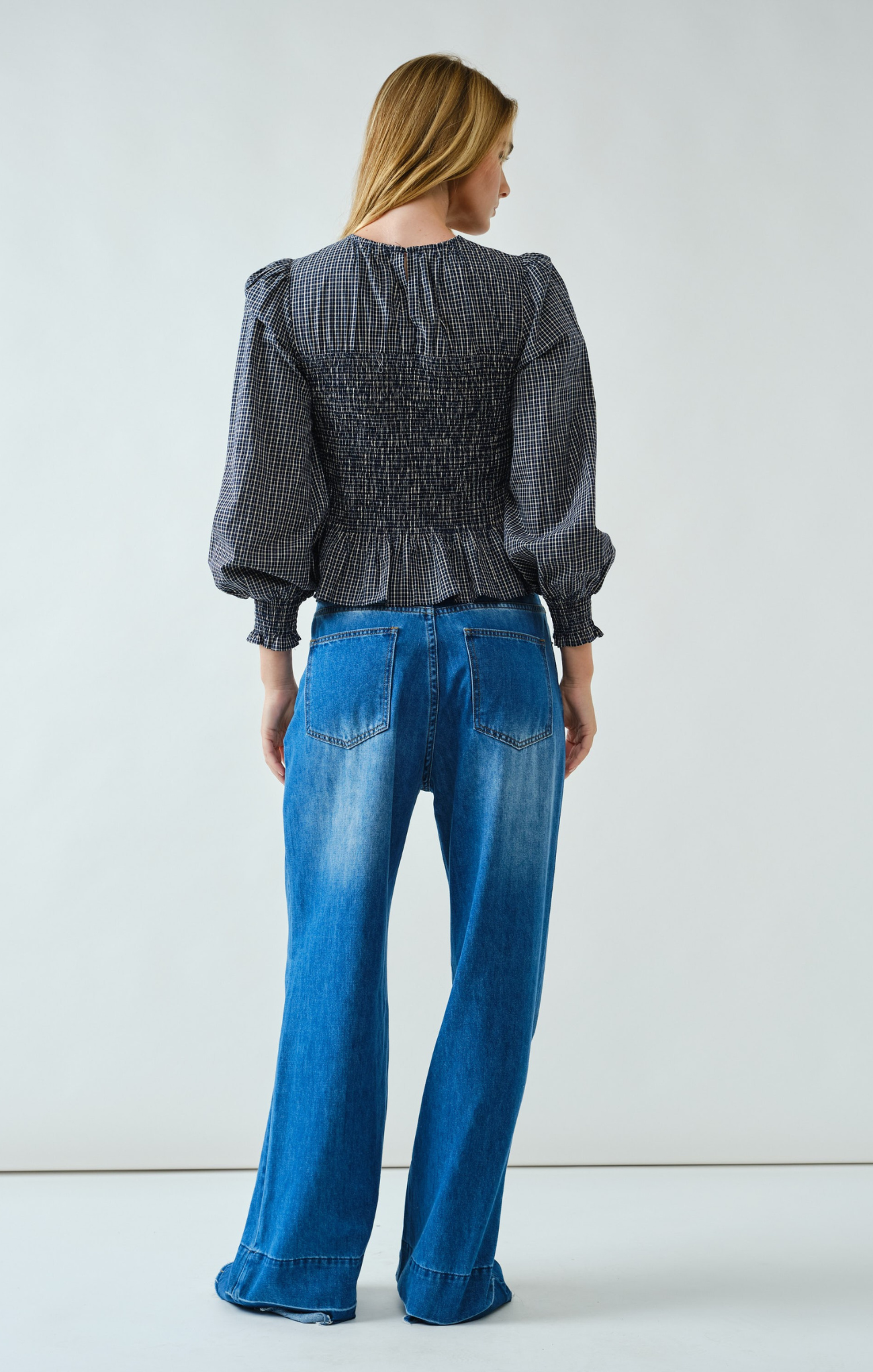 Woman wearing a dark patterned blouse and blue jeans against a white background