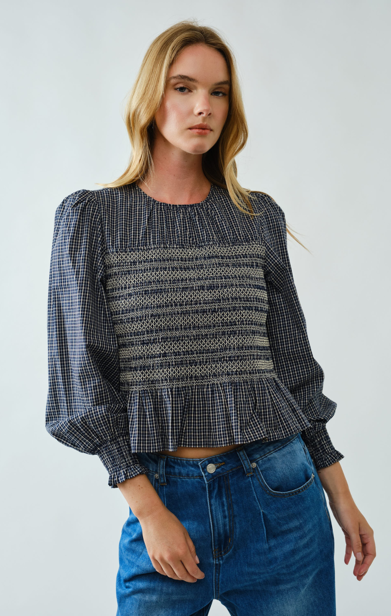 Woman wearing a patterned blouse and blue jeans against a plain background