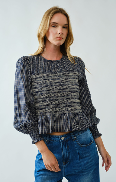 Woman wearing a patterned blouse and blue jeans against a plain background