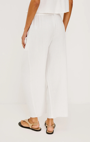 Person wearing white pants and sandals on a plain background