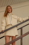 Woman in a cream-colored outfit standing on a staircase.