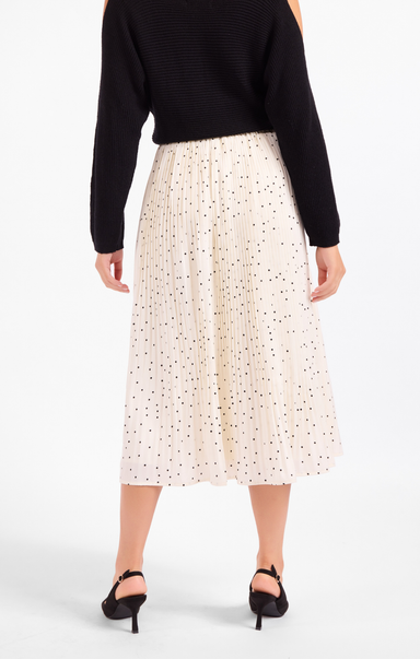Person wearing a black top and white skirt with black polka dots on a white background