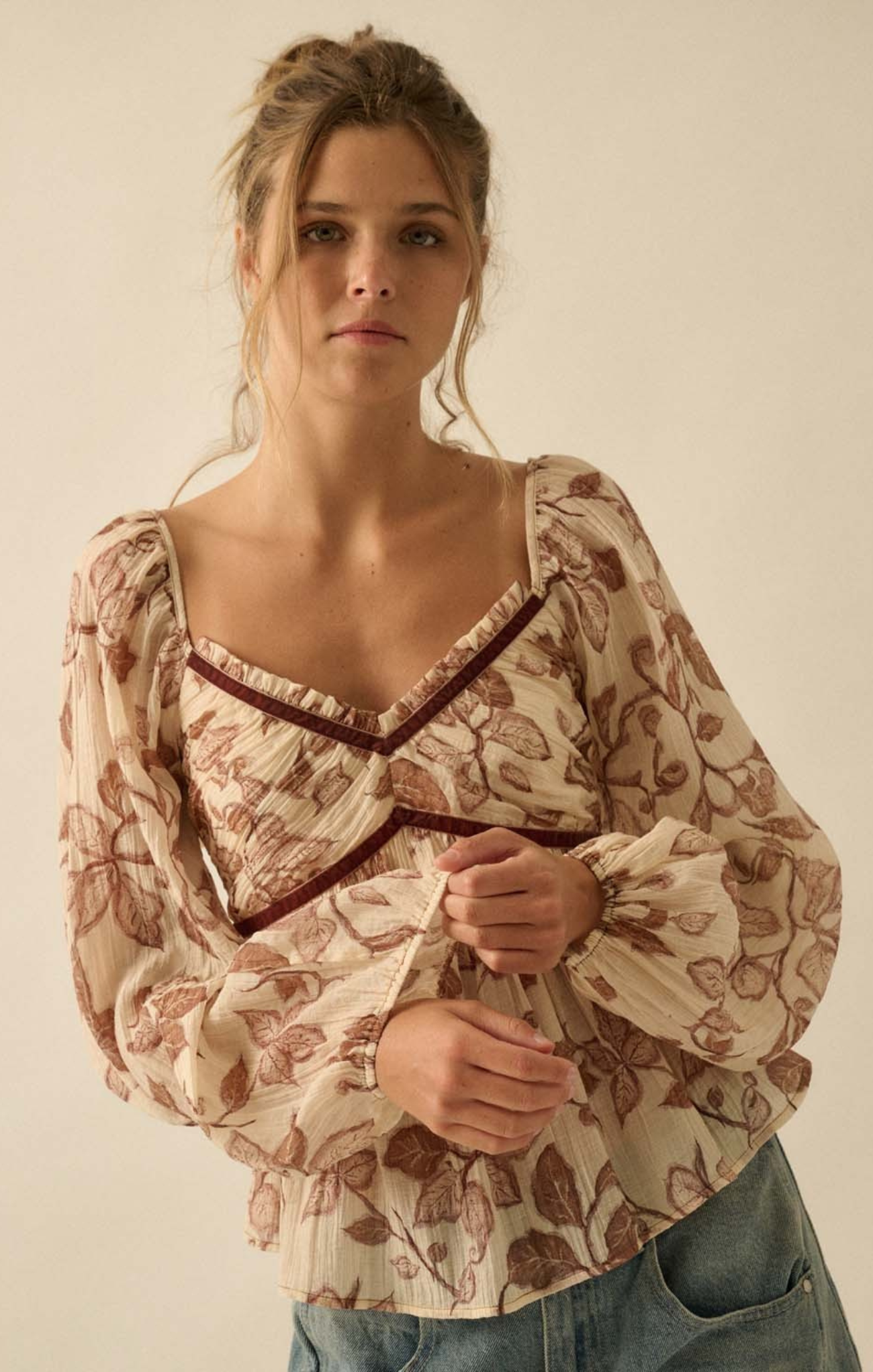 Woman wearing a patterned blouse with long sleeves against a plain background