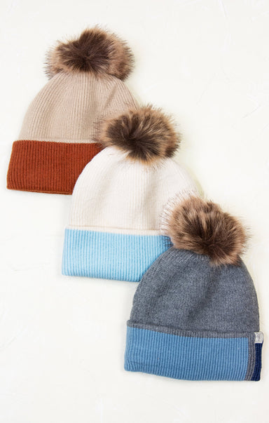 Three color-blocked beanies with pom-poms on a white background