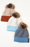 Three color-blocked beanies with pom-poms on a white background