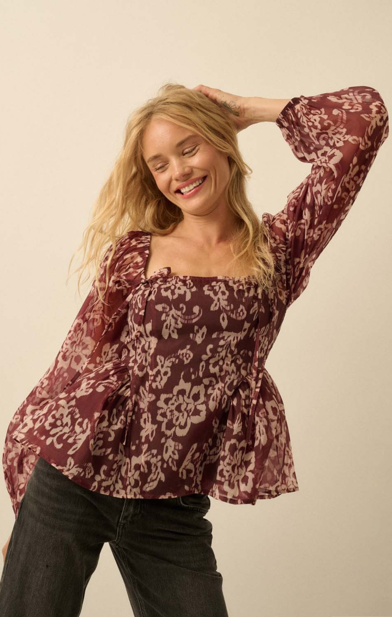 Woman wearing a burgundy floral blouse against a beige background