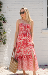 Woman wearing a red floral dress standing in front of a white brick wall.