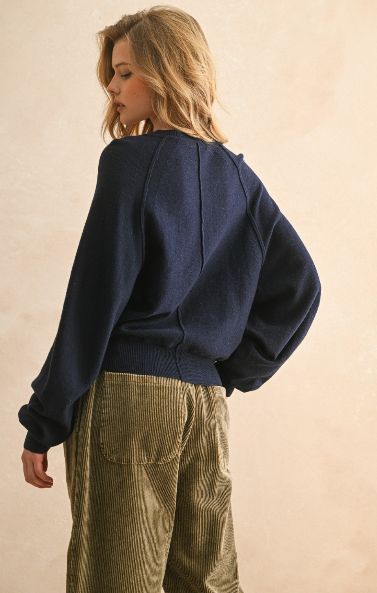 Person wearing a navy blue sweater and beige pants against a plain background