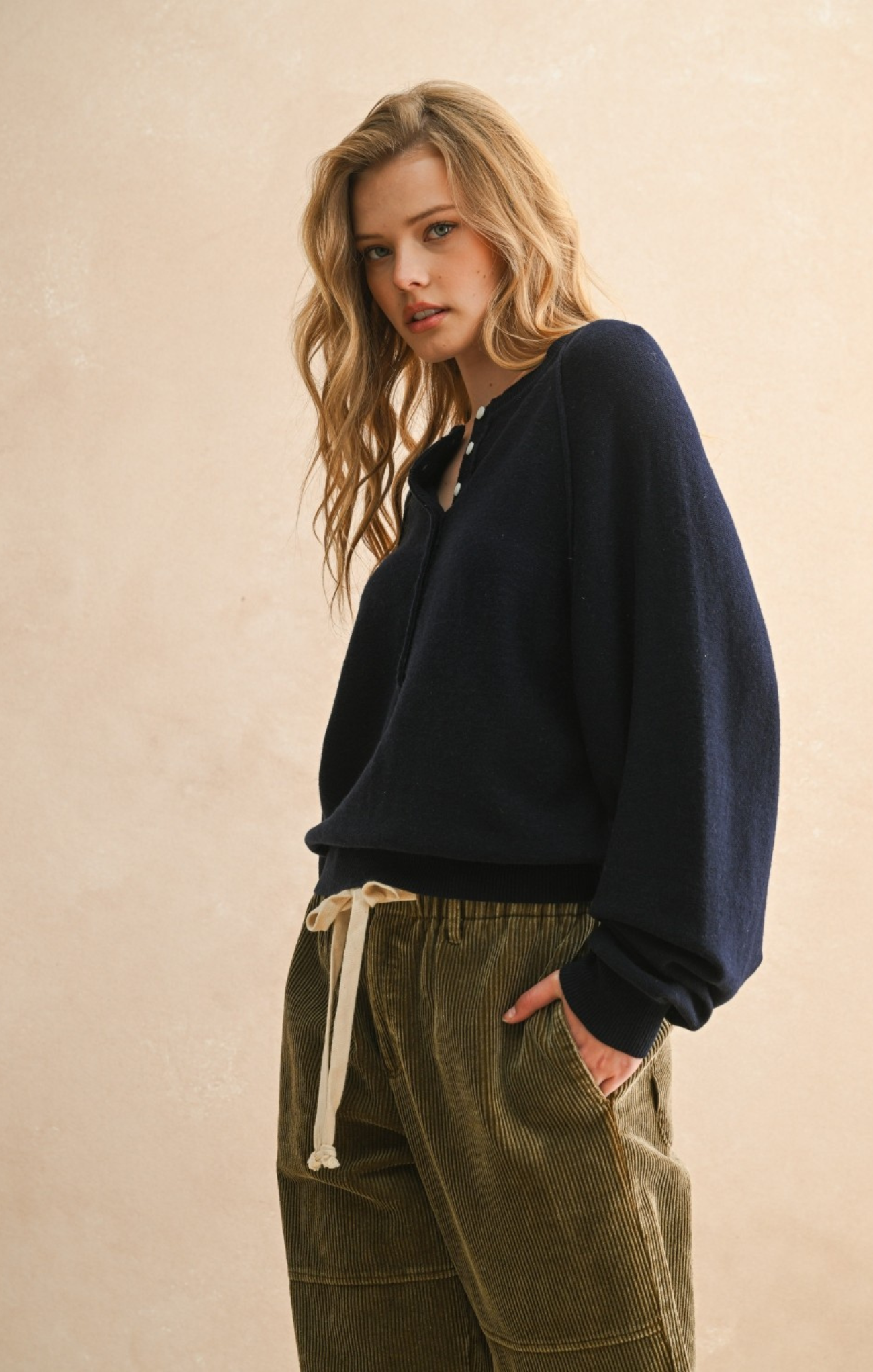 Woman wearing a navy sweater and green pants against a beige background