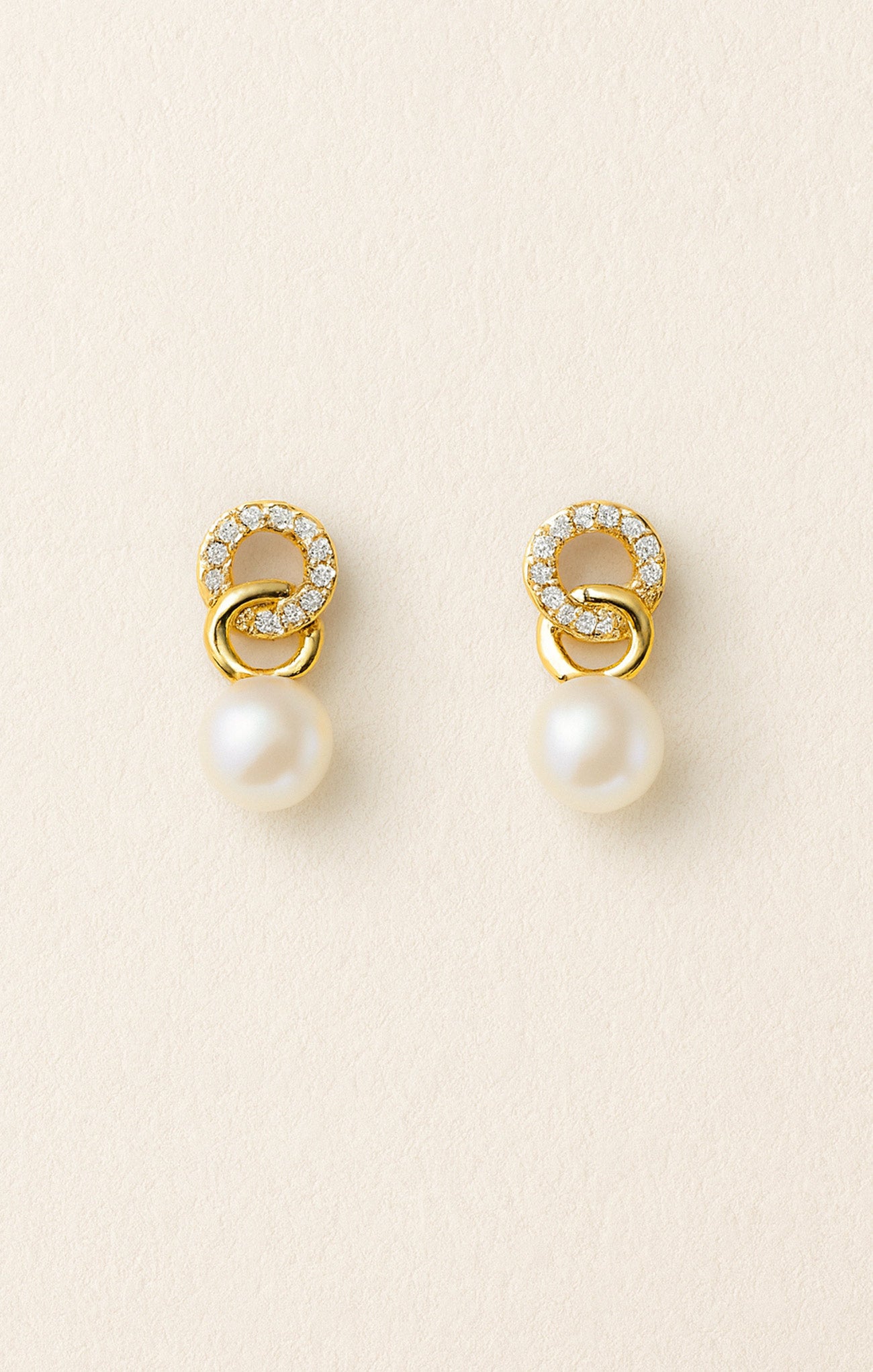 Pair of gold earrings with pearls on a beige background