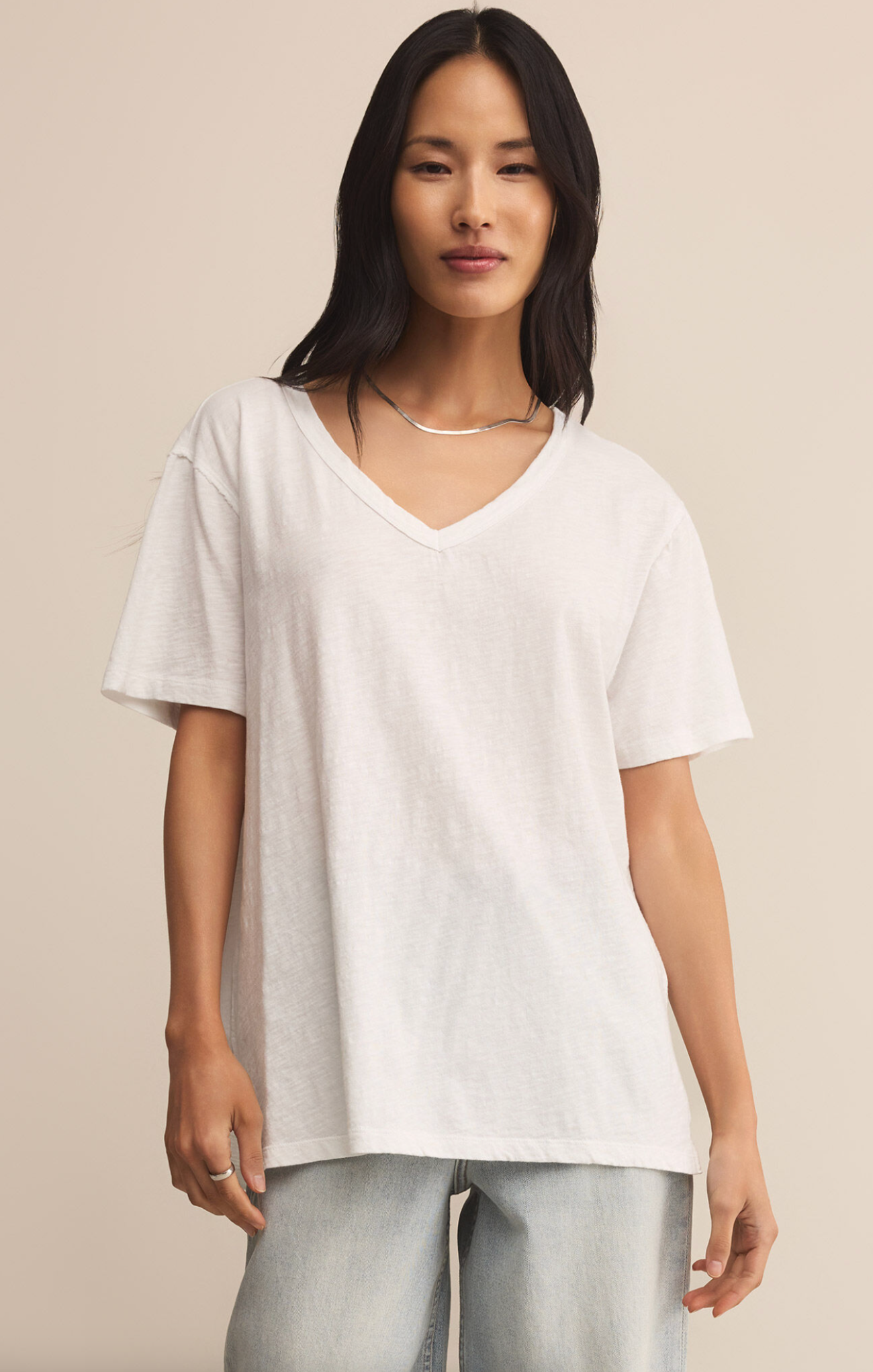 Woman wearing a white t-shirt and light blue jeans against a beige background