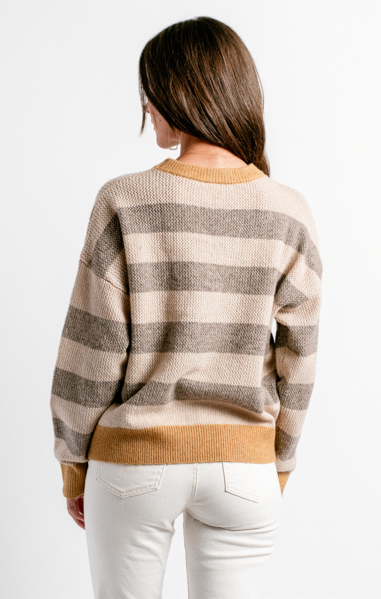 Woman wearing a striped sweater with a neutral color palette on a white background