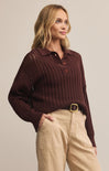 A woman wearing a brown collared long sleeve button front polo sweater with a relaxed fit, paired with beige pants.