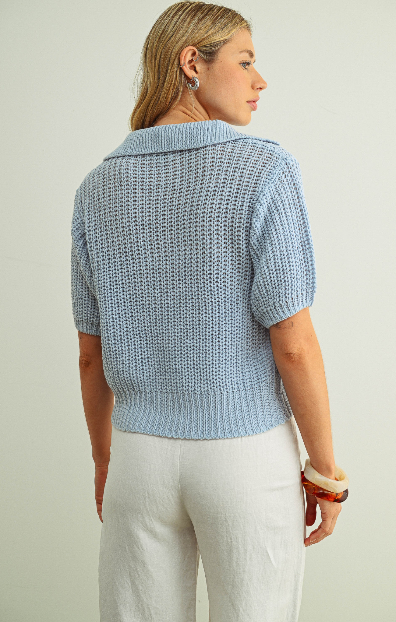 Woman wearing a light blue knitted cardigan over a white top against a plain background