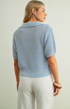 Woman wearing a light blue knitted cardigan over a white top against a plain background