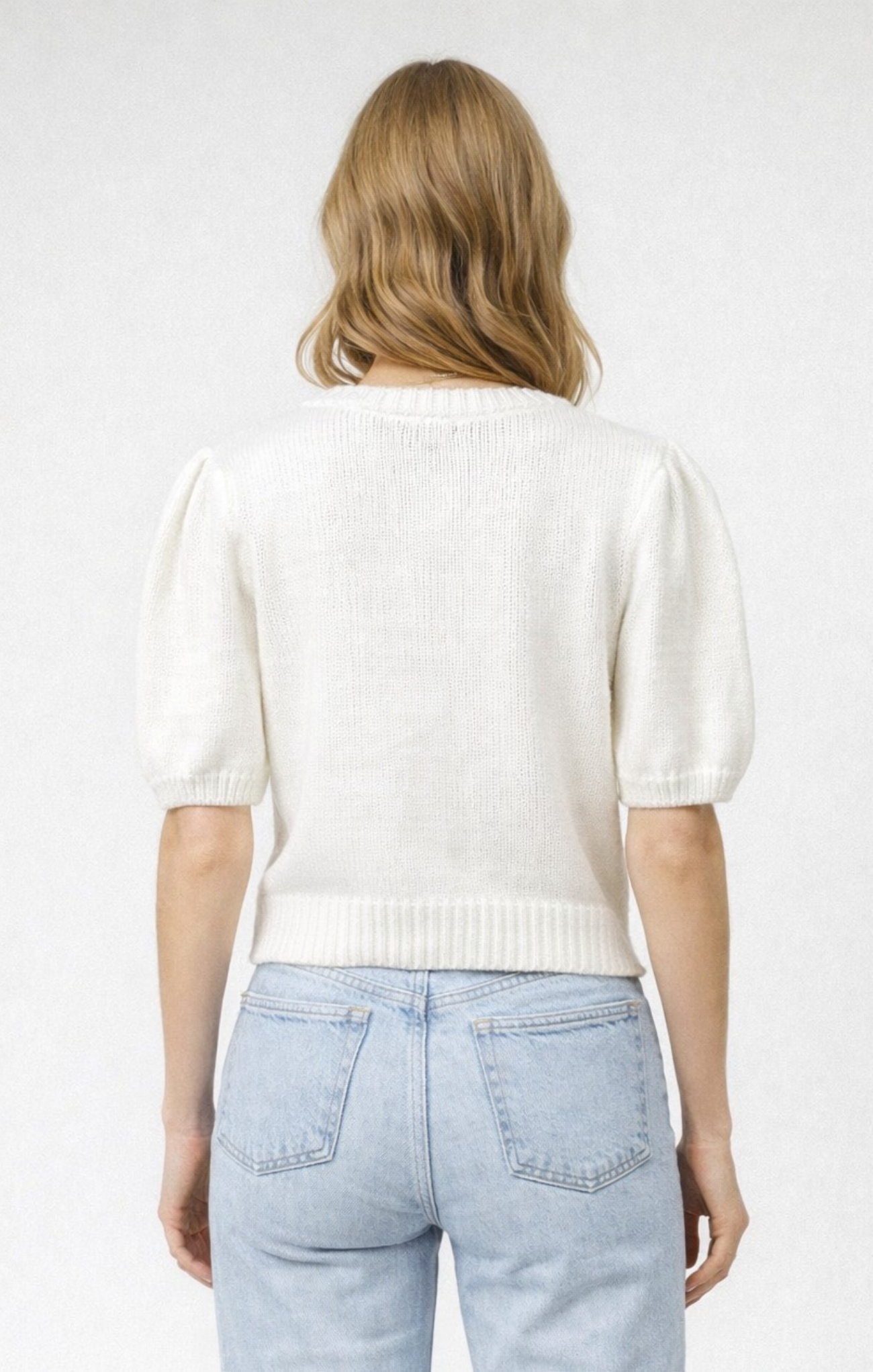 Person wearing a white knit sweater and light blue jeans on a plain background