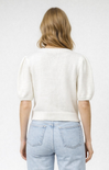 Person wearing a white knit sweater and light blue jeans on a plain background