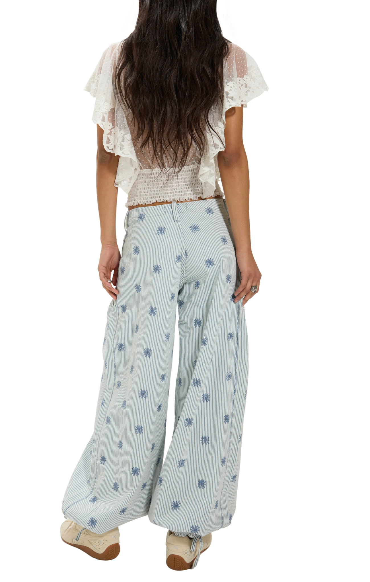 Woman wearing a white lace top and light blue patterned pants on a white background