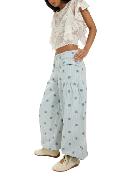 Person wearing light blue floral-patterned pants and a white lace top on a white background