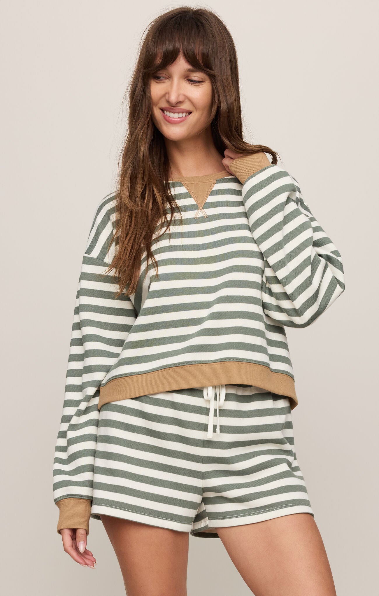 Woman wearing a green and white striped outfit with a beige waistband on a plain background