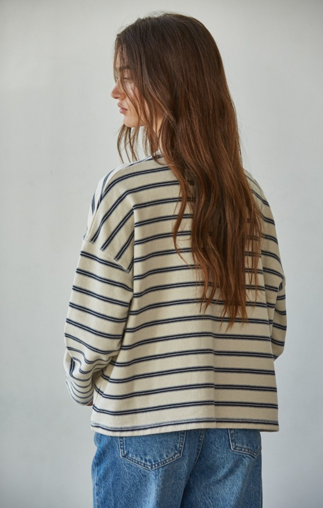 Person wearing a striped sweater and jeans against a plain background