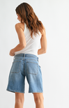Woman wearing denim shorts and a white tank top on a plain background