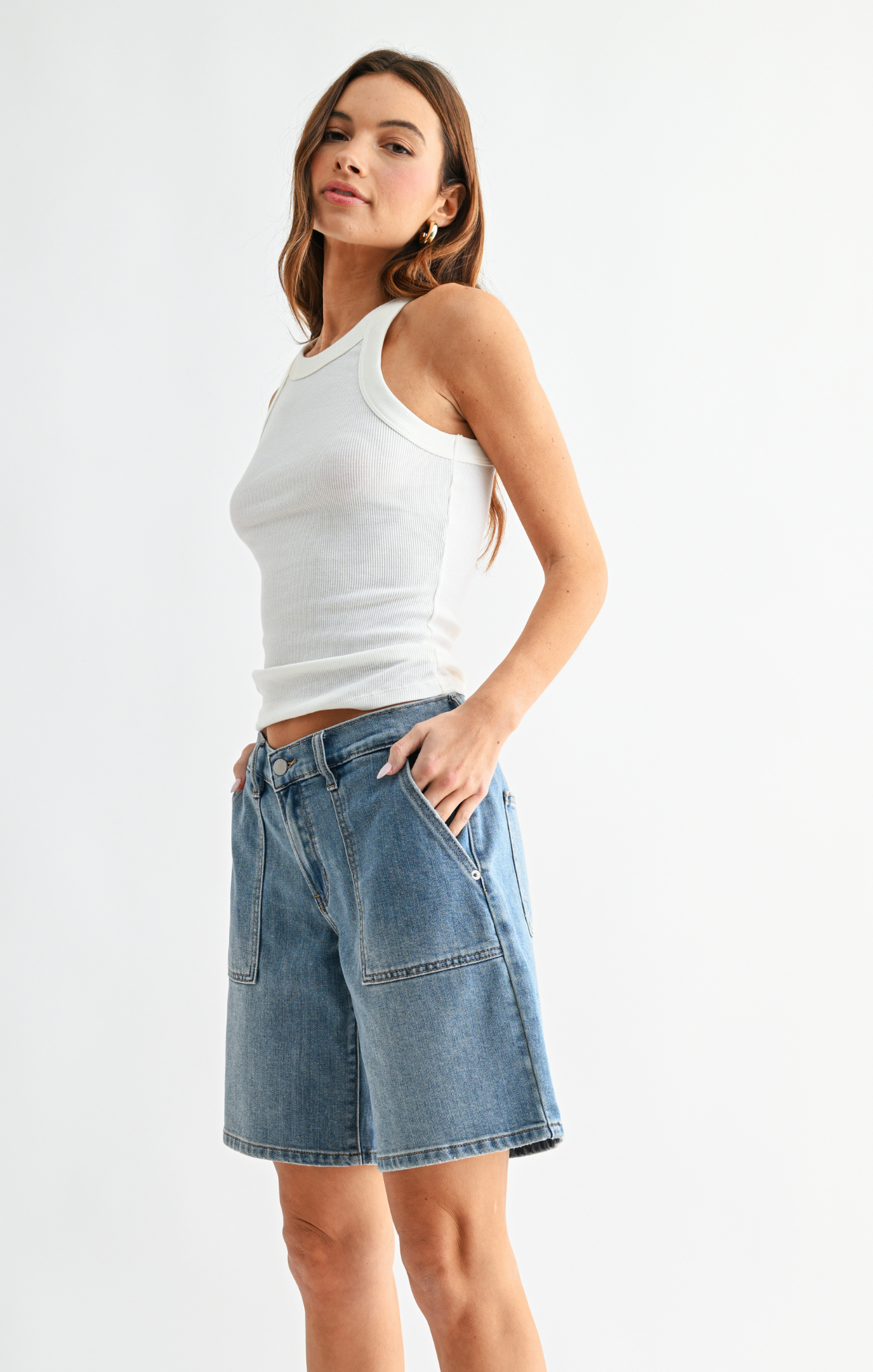 Woman wearing a white tank top and denim shorts on a white background
