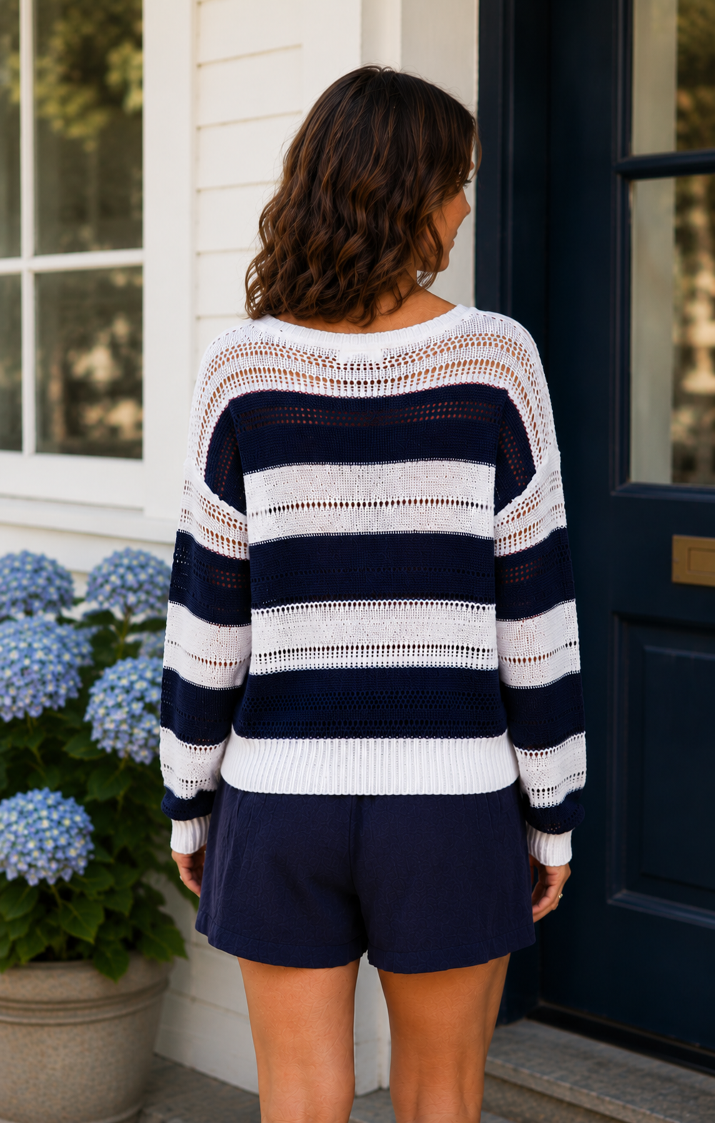 Woman wearing a navy and white striped sweater and shorts standing in front of a door.
