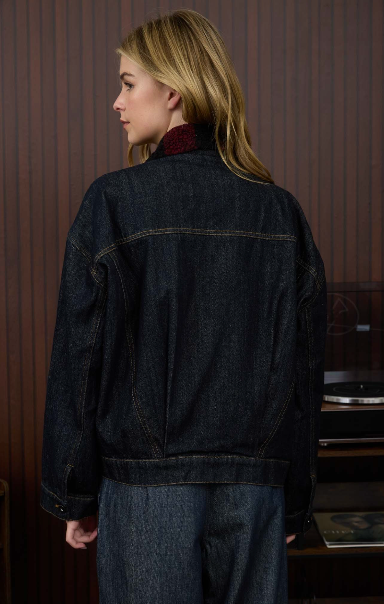 Person wearing a dark denim jacket in a room with wooden paneling.