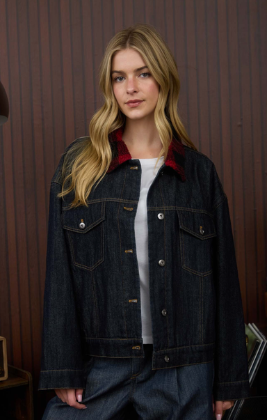 Woman wearing a dark denim jacket with a red interior lining against a wooden paneled wall.