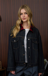 Woman wearing a dark denim jacket with a red interior lining against a wooden paneled wall.