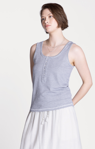 Woman wearing a striped tank top and white pants on a plain background