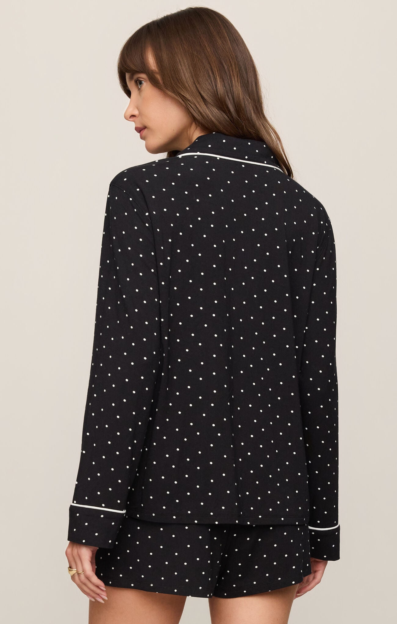 Woman wearing a black polka dot pajama set with white piping on a beige background