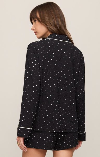 Woman wearing a black polka dot pajama set with white piping on a beige background