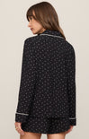 Woman wearing a black polka dot pajama set with white piping on a beige background