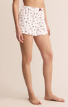 White pajama shorts with red floral pattern worn by a person on a beige background