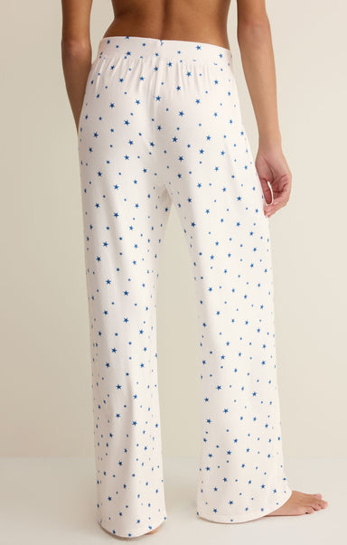 White pajama pants with blue star pattern worn by a person on a beige background