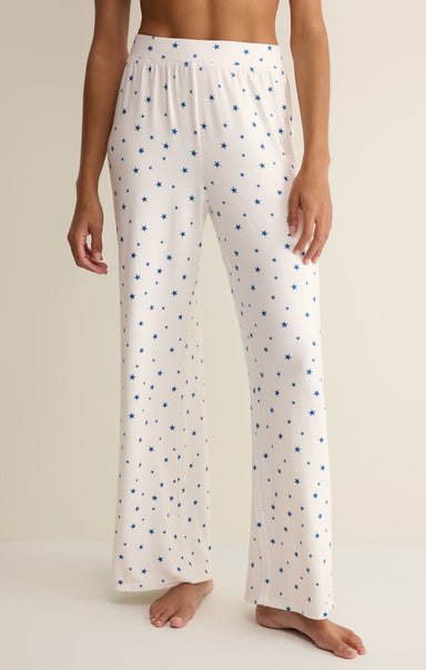 White pajama pants with blue star pattern worn by a person on a beige background