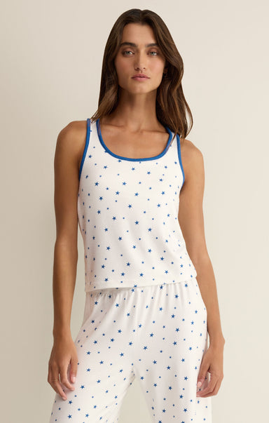 Woman wearing a white sleeveless top with blue star pattern and matching pants on a beige background