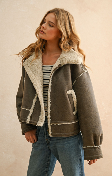 Woman wearing a brown jacket with white fur lining against a beige background