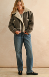 Woman wearing a brown shearling jacket and blue jeans against a beige background