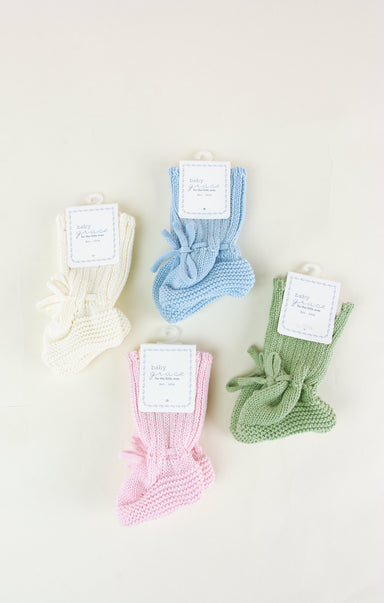 Four pairs of knitted baby socks in white, blue, pink, and green on a light background.
