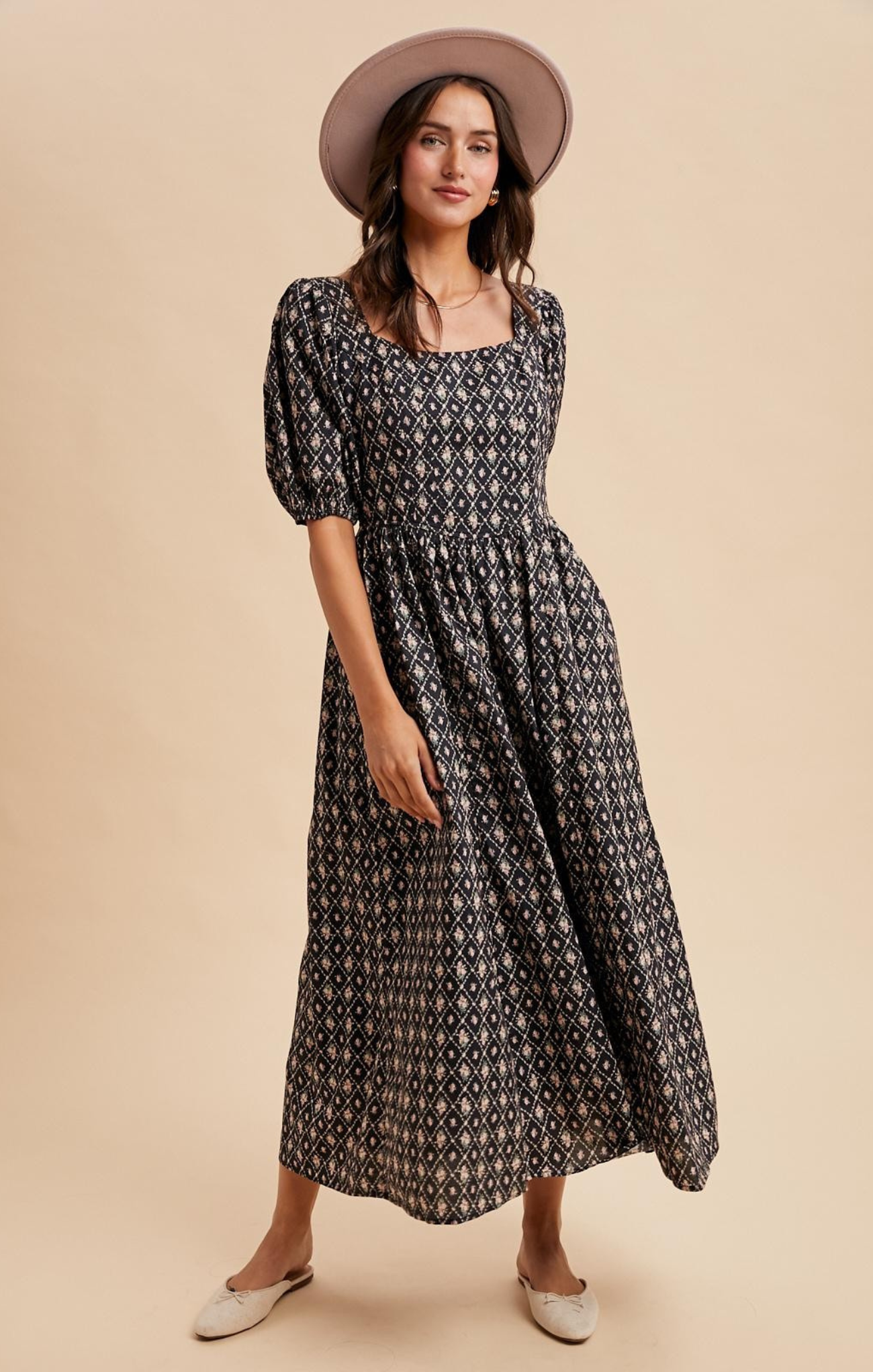 Woman wearing a black patterned dress and beige hat on a beige background