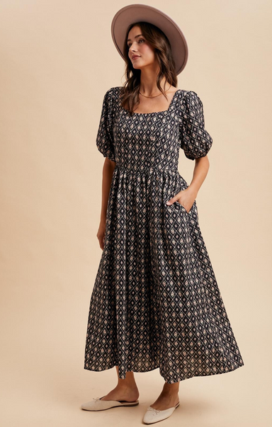 Woman wearing a black patterned dress with puff sleeves and a brown hat on a beige background