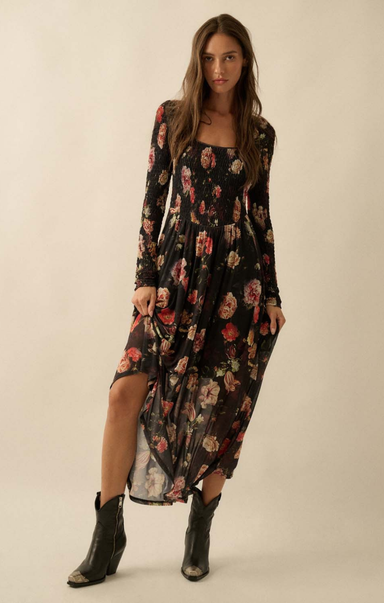 Woman wearing a floral dress with a high slit and black boots on a plain background